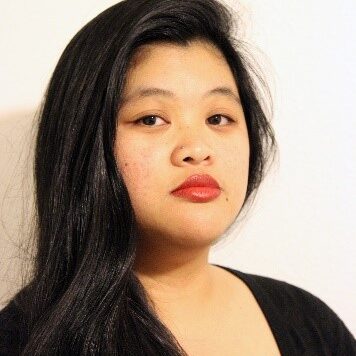 A Filipina woman with long black hair, looking into the camera with a serious expression wearing a black blouse.