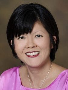 An Asian American woman with short black hair and bangs smiling in a pink blouse.