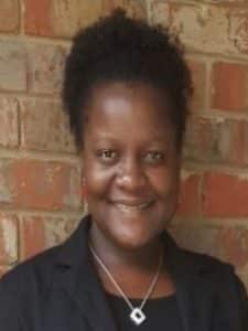 A Black woman with natural hair in a high ponytail smiling and wearing a black blazer and blouse.