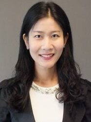 A Korean woman smiling with long, black hair parted in the middle, wearing a white blouse with a blazer.